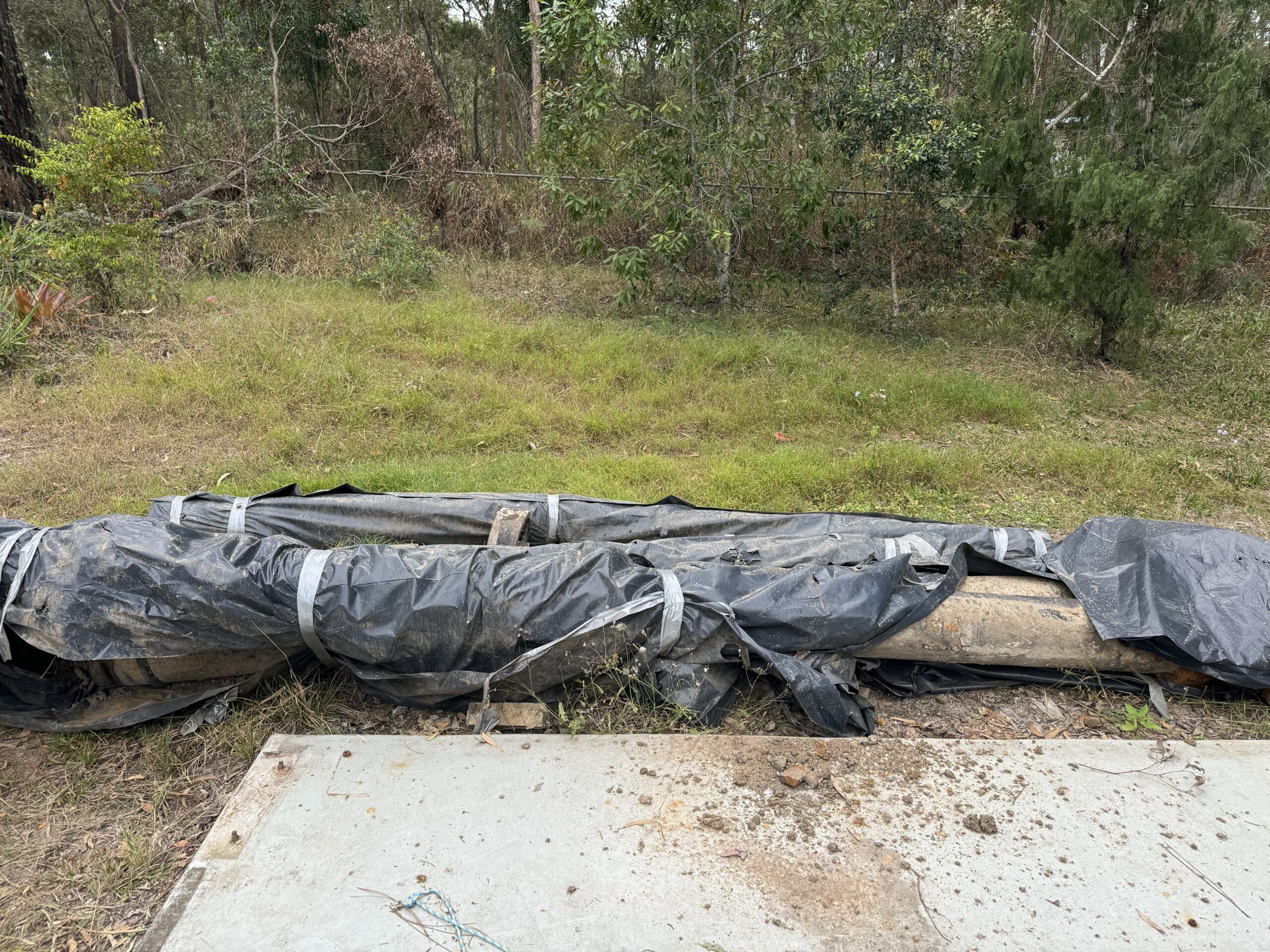 Asbestos cement water main pipe partially sealed and bagged for regulated waste disposal.