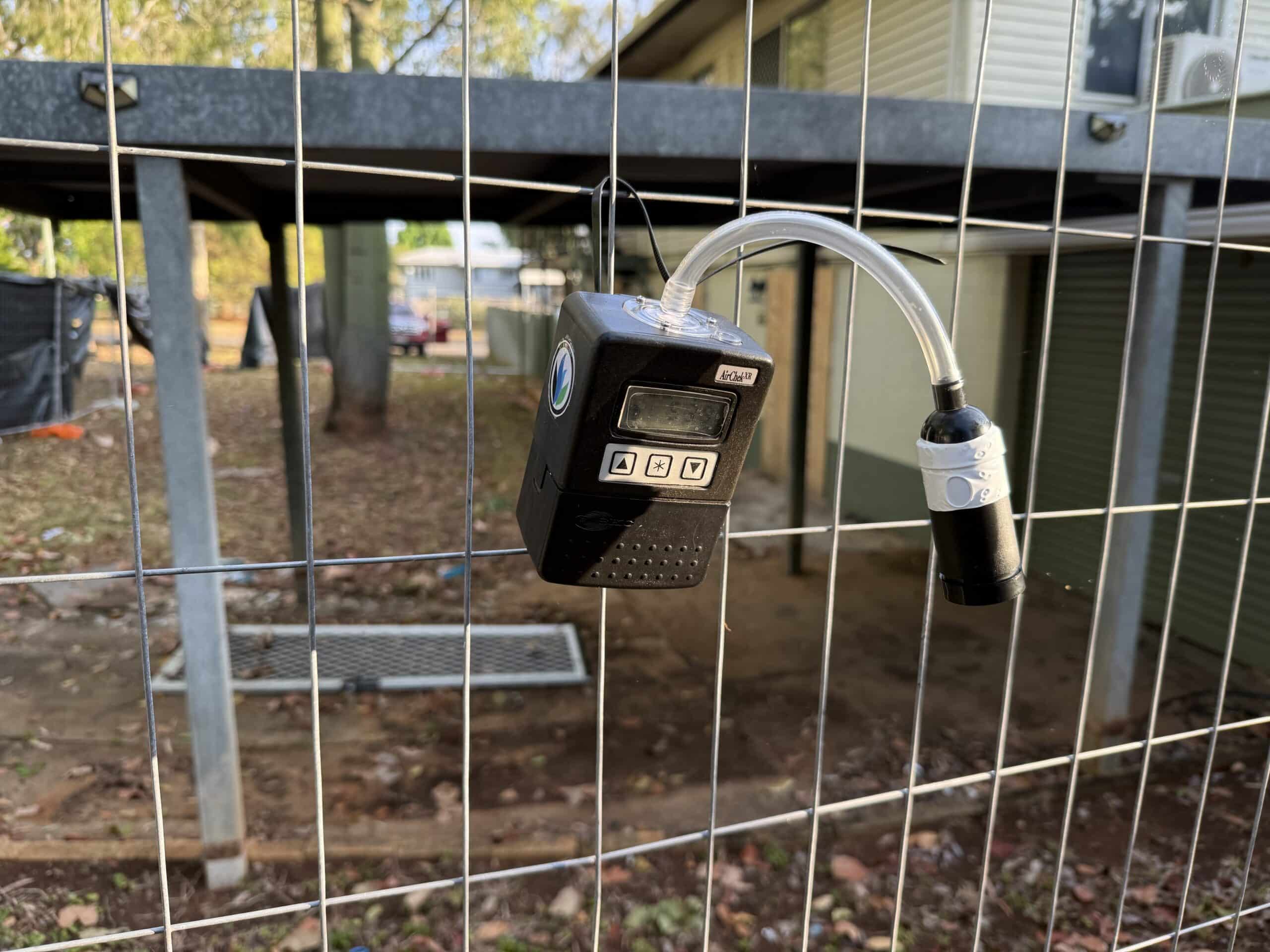 Air monitoring pump mounted on temporary fencing at a construction site