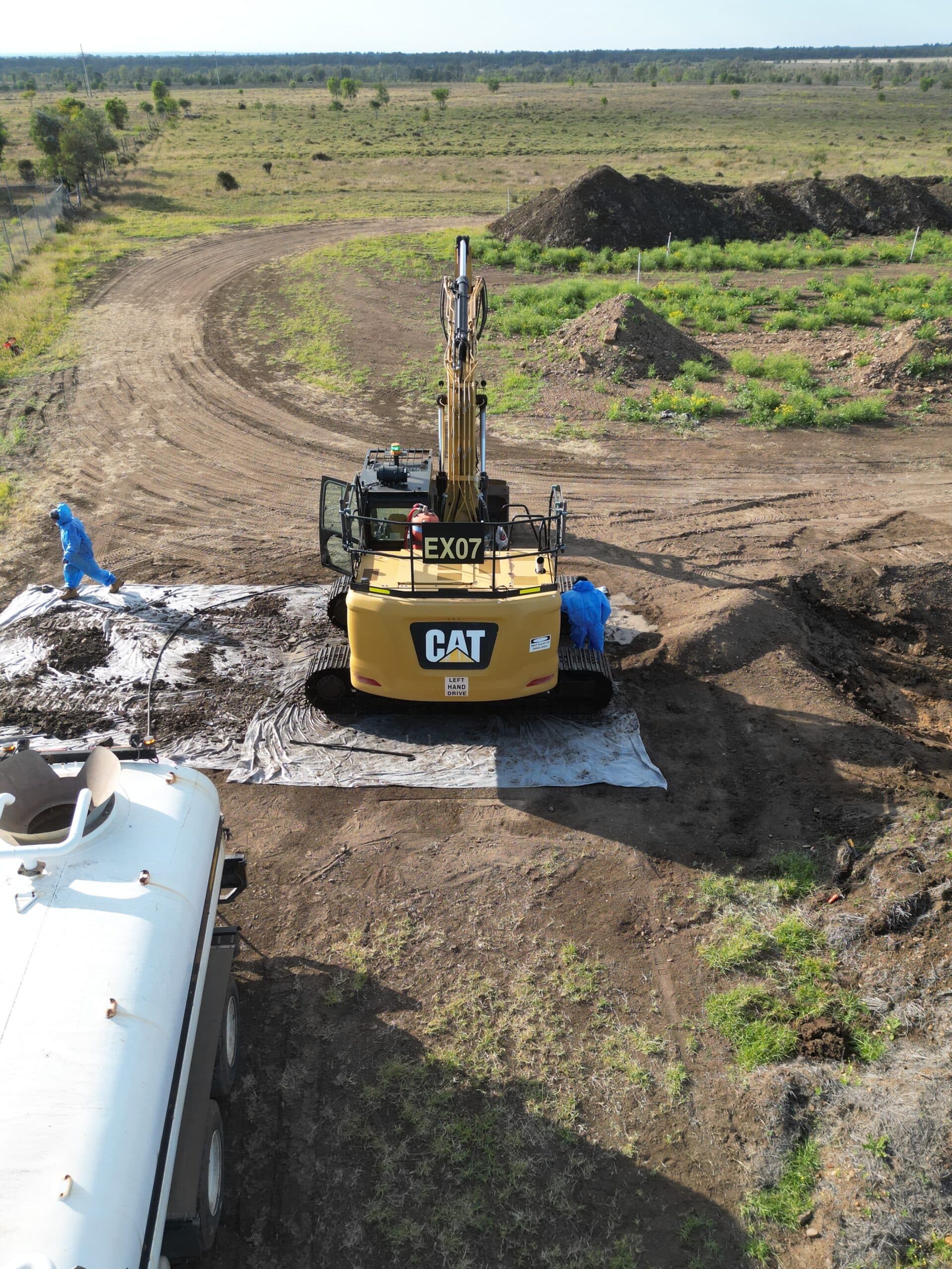 Aerial view of an excavator and workers in protective suits remediating contaminated soil on a regulated waste site